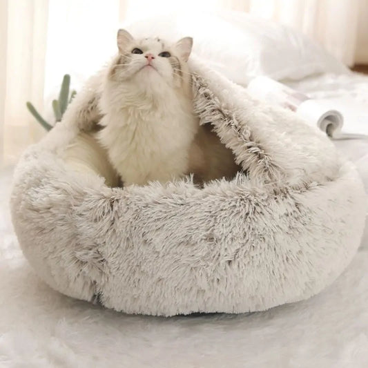 white kitten sits in a grey snuggle bed in a home setting. 