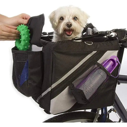 small white dog in a pet bicycle basket carrier, a person's hands are shown putting toys in the side pockets of the basket. white background. 