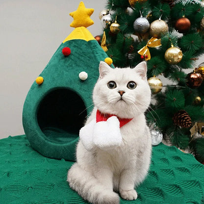 A white cat sits next to the Christmas Cat Bed in a home setting, next to a Christmas Tree. 
