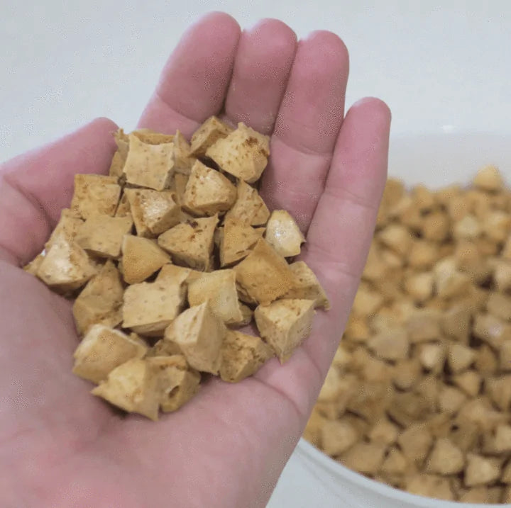 a hand full of homemade dog treats is in the foreground, a bowl of treats in the background. 