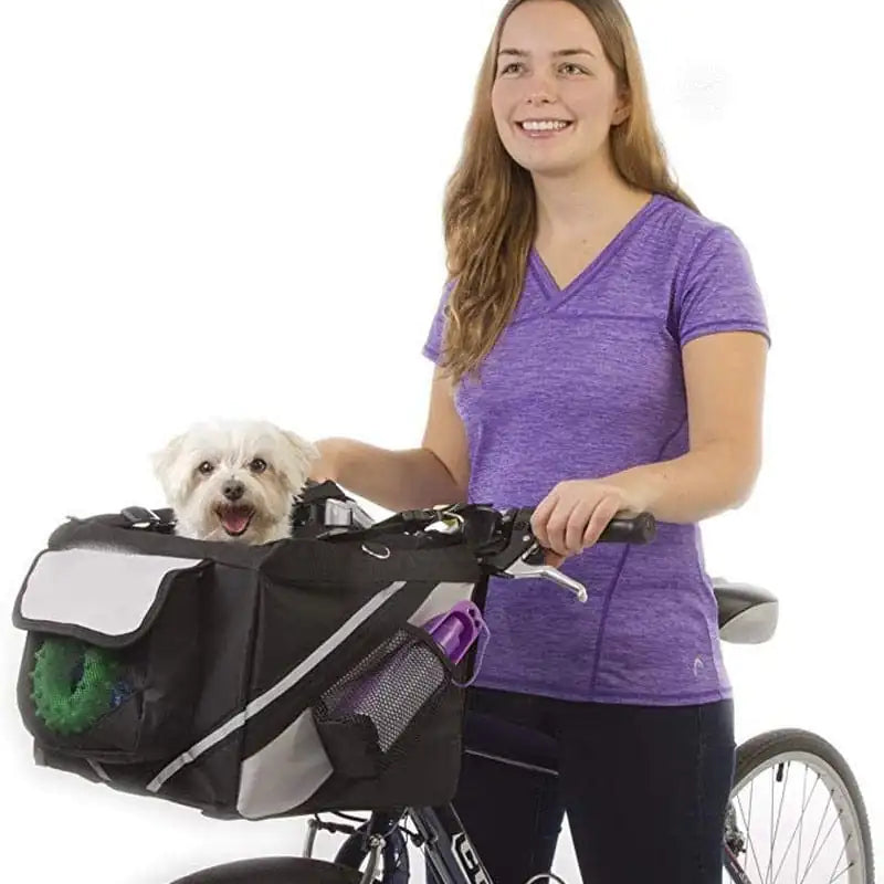 woman wearing a purple shirt, black tights, holding a pushbike, with a black pet bicycle basket carrier attached, with a small white dog inside. white background