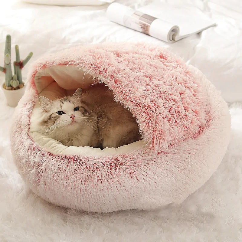 a kitten lies in a pink snuggle bed in a home setting