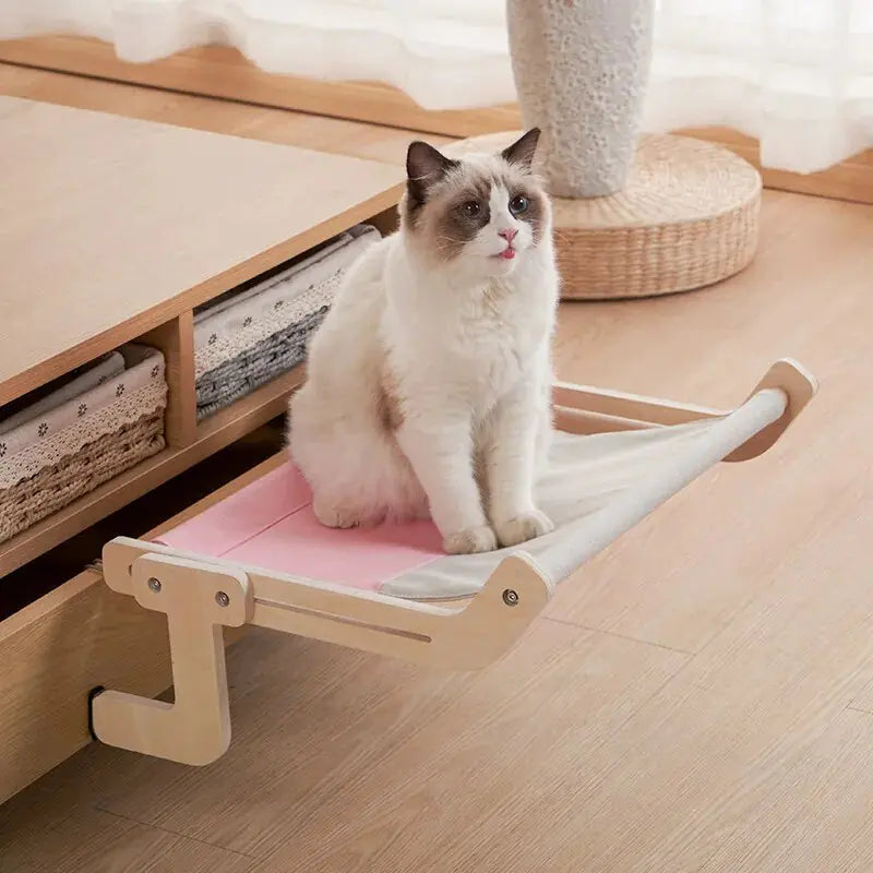 A white cat sits on a pink Feline Window Perch in a home setting