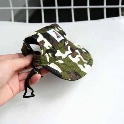 Camo pattern Pet  Baseball Cap in a person's hand against a white and black background. 