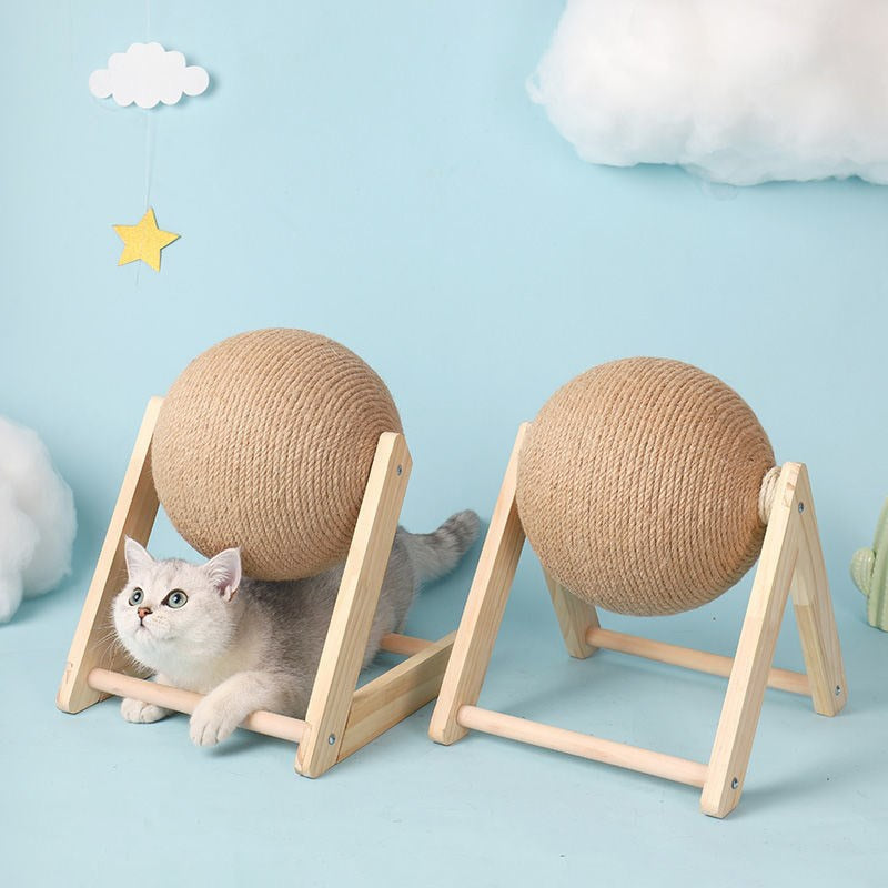 two cat scratch balls side by side in a studio staged setting,  blue background, white cottonwool clouds and a yellow paper star form the backdrop. The two scratching balls show the different style wooden bases available. There is a silver and white cat lying under one of the balls, looking up. 