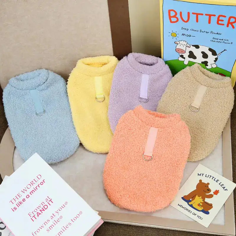 In a home setting, the five different colored sweaters are displaying the back view, with leash attachment strap. There are children's books in the scene. 