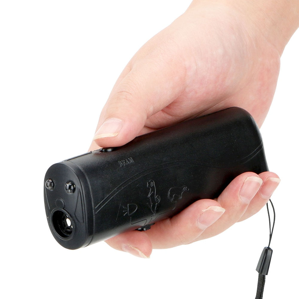 A black hand-held device is held by a person, showing the wrist strap hanging. The person's thumb is positioned over the on/off button, and the torch feature is clearly visible.