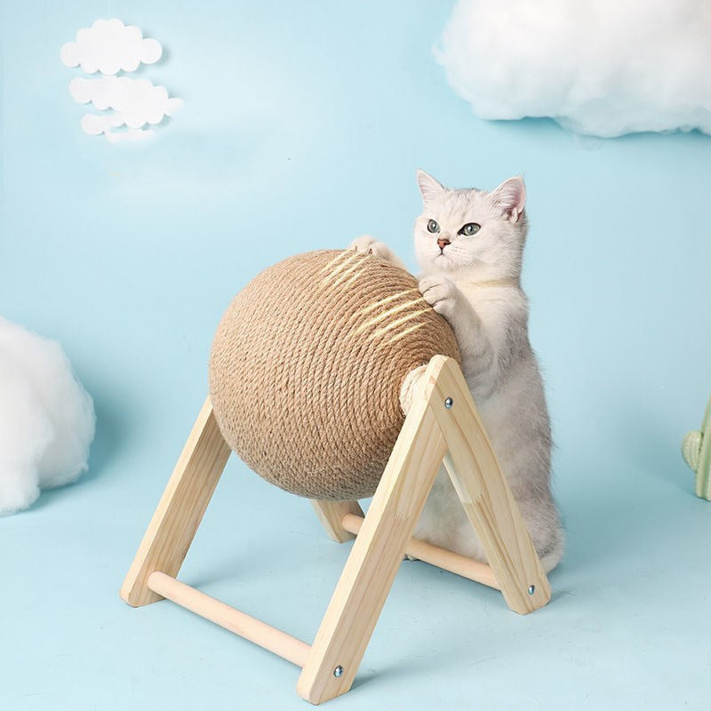 Studio shot of silver and white cat standing with front paws on cat scratching ball, with pretend scratch marks on the ball. White cottonwool clouds are staged in the background. 